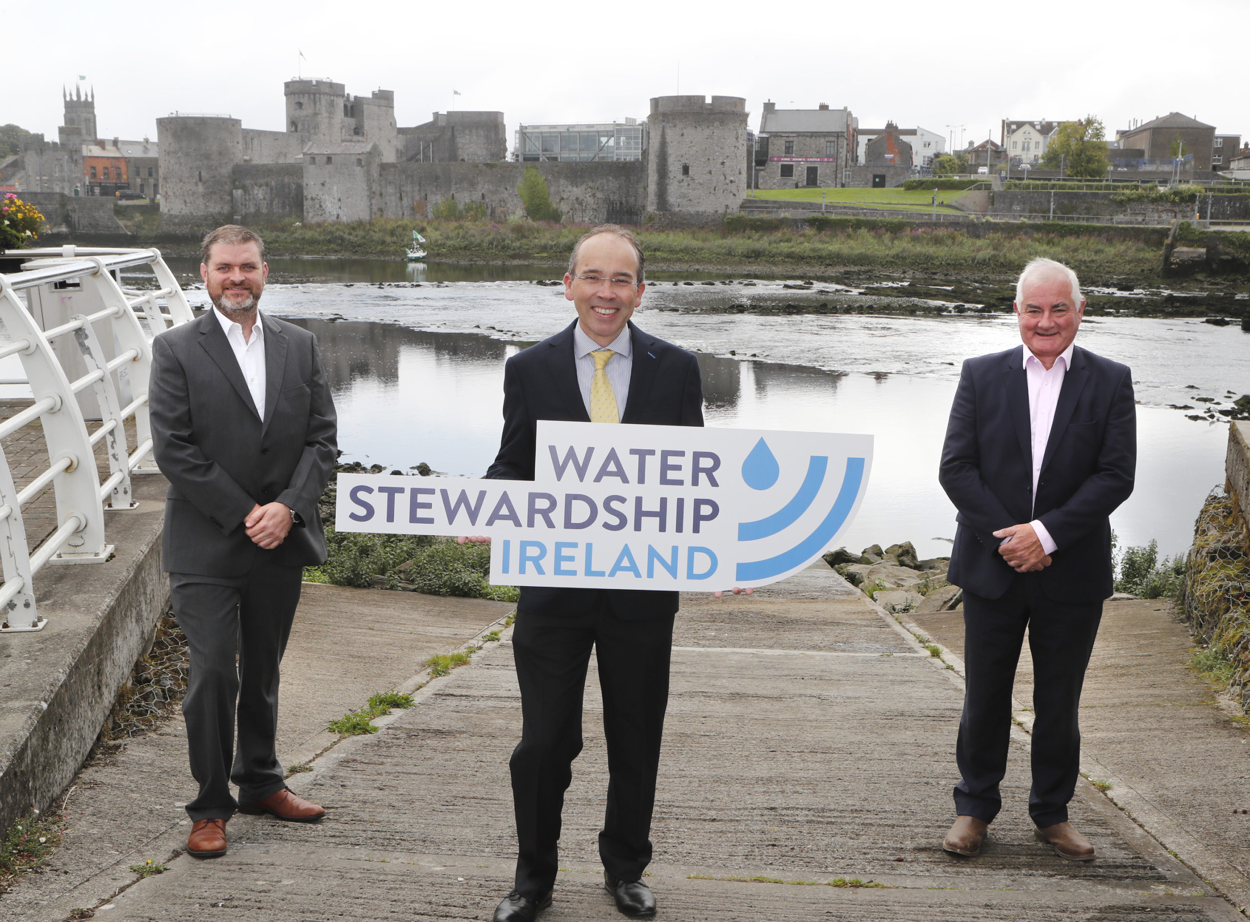 Three men standing together - one of them holding a sign that says "Water Stewardship Ireland".